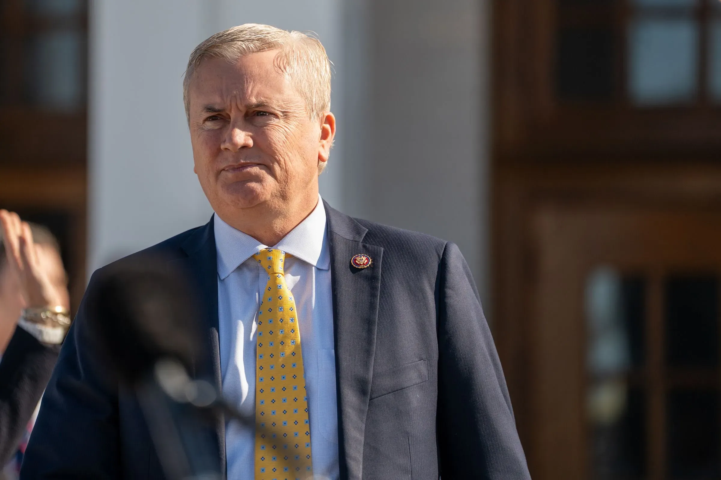 رجل يرتدي بدلة رسمية مع ربطة عنق صفراء، يبدو جادًا وهو يتحدث في حدث رسمي، في سياق فضيحة الاحتيال في الرعاية الاجتماعية بمينيسوتا.