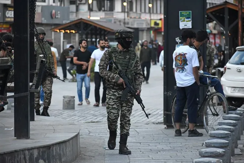 جنود يرتدون زيًا عسكريًا ويحملون أسلحة في منطقة حضرية، بينما يتجول مدنيون في الخلفية، مما يعكس التوترات الأمنية بين الهند وباكستان.