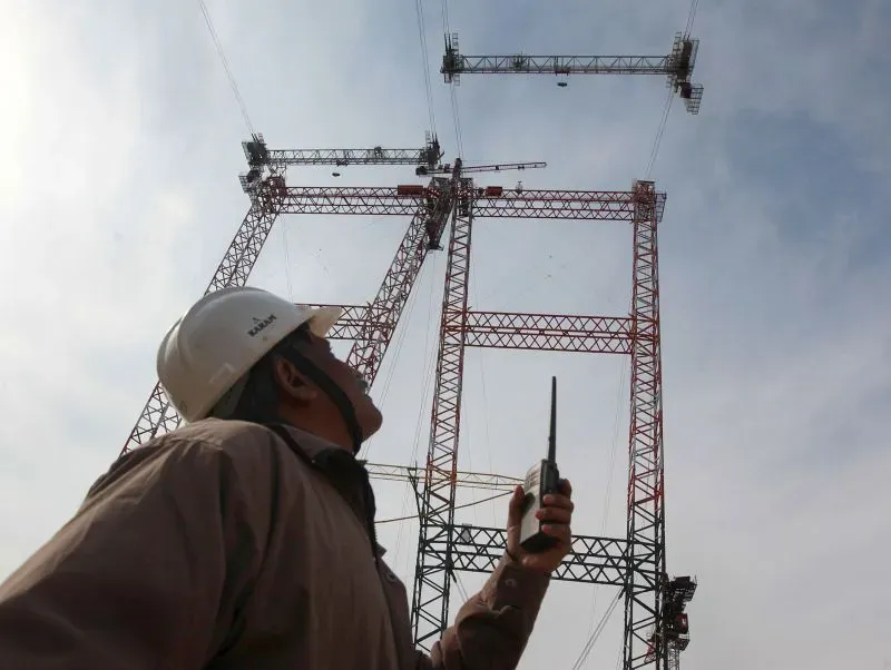 عامل بناء يرتدي خوذة ويستخدم جهاز اتصال لاسلكي، يتابع أعمال بناء جسر تشيناب في كشمير، الذي يُعتبر الأعلى عالمياً.