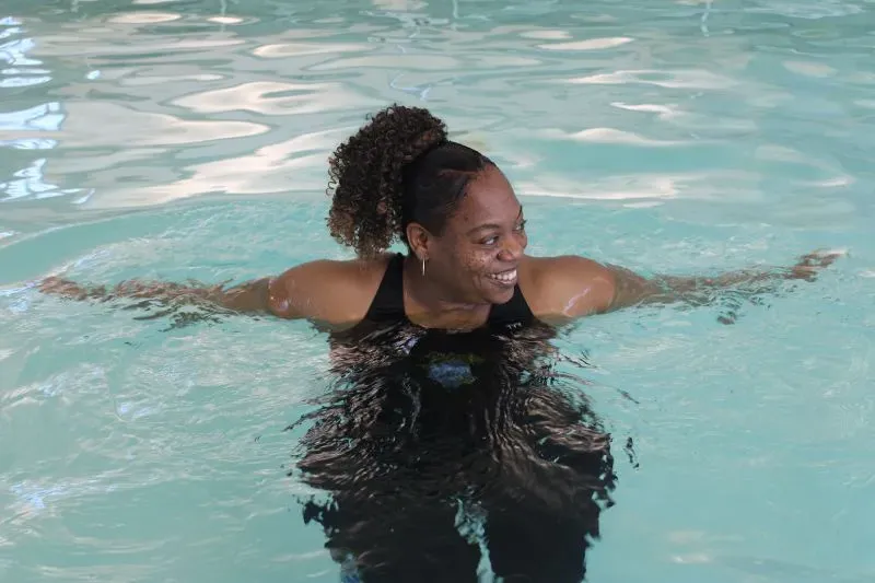 امرأة مبتسمة تسبح في حمام سباحة، تعكس روح التفاؤل والثقة. الصورة تعبر عن أهمية تعليم السباحة وتعزيز المشاركة بين الأطفال السود.