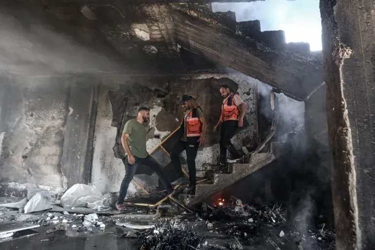 رجال إنقاذ يرتقون الدرج في مبنى مدمر بعد الهجمات الإسرائيلية على غزة، مع وجود دخان وحطام حولهم.