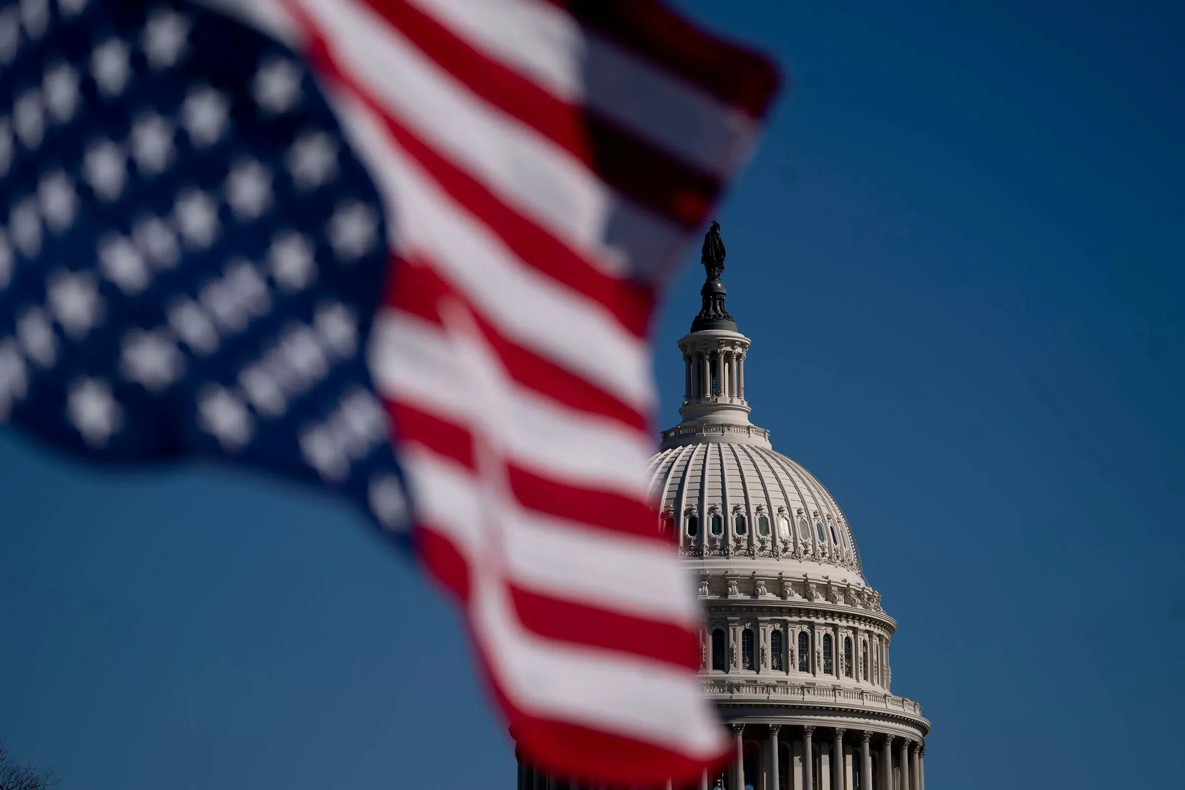علم الولايات المتحدة يرفرف أمام قبة مبنى الكابيتول، مما يرمز إلى حالة السياسة الأمريكية الحالية والتحديات التي تواجهها.