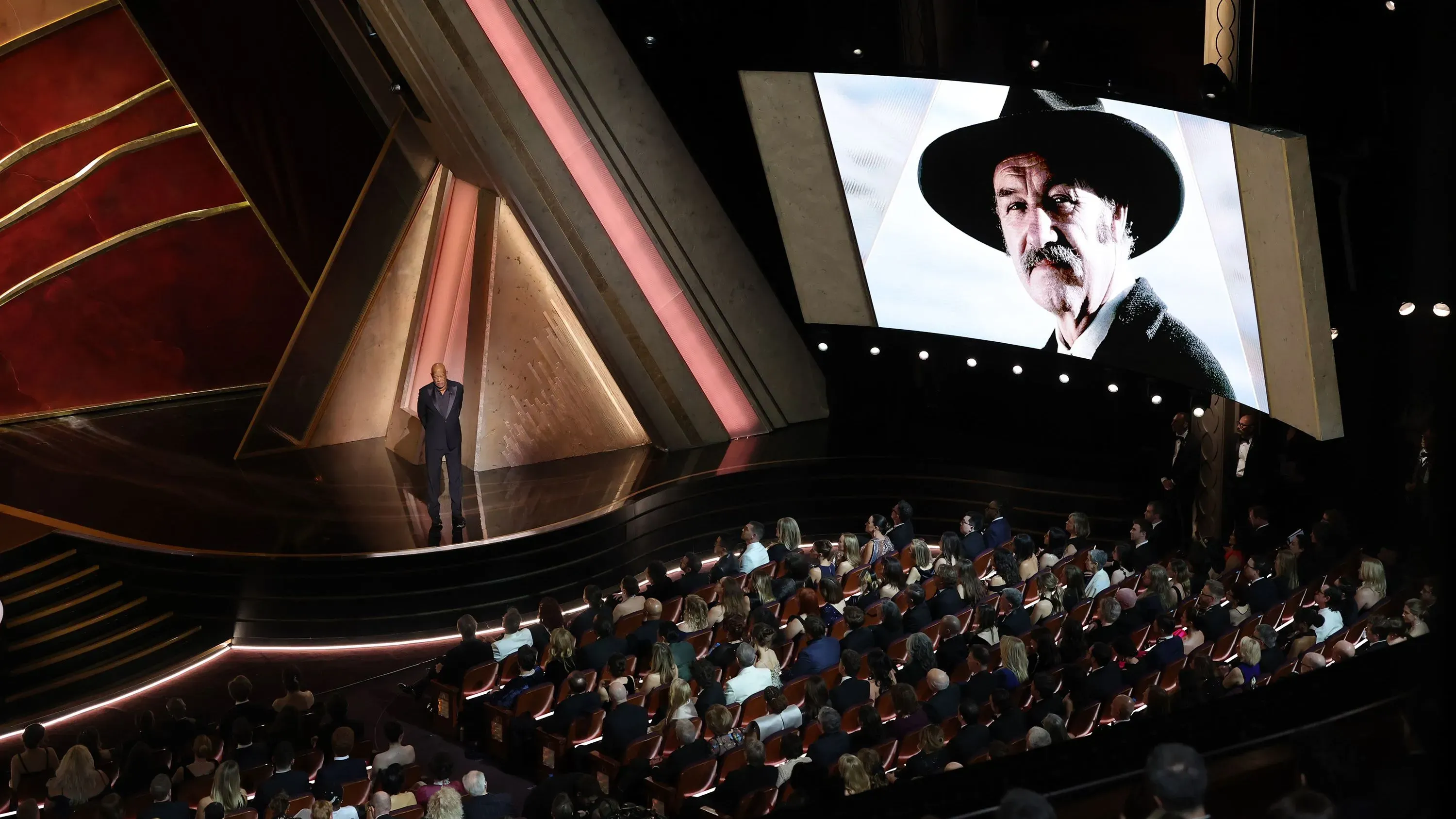 تقديم تكريم مؤثر لجين هاكمان من قبل مورغان فريمان خلال حفل توزيع جوائز الأوسكار، مع صورة لهاكمان على الشاشة.