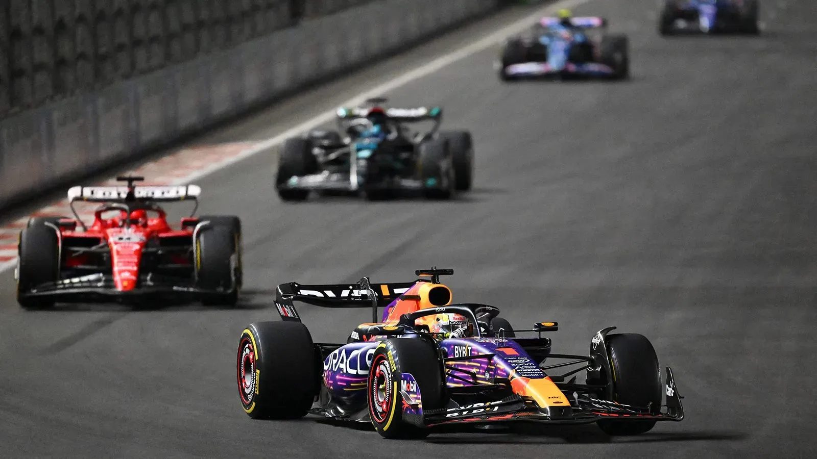 سيارة فورمولا 1 تتصدر السباق مع سيارات أخرى تتنافس خلفها على حلبة، تعكس أجواء المنافسة في رياضة السيارات.