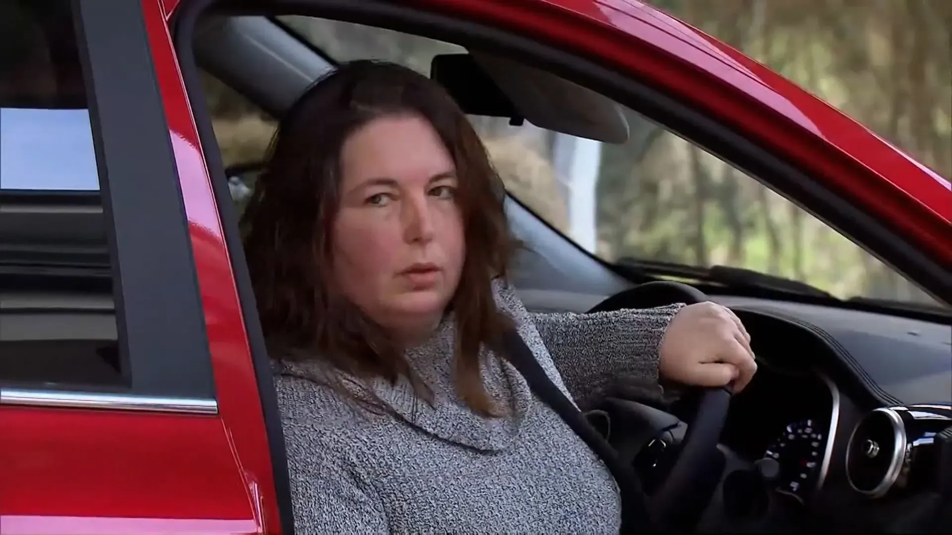 إيرين باترسون، المتهمة بقتل ثلاثة من أقاربها بفطر سام، تجلس في سيارة حمراء بينما تتابع مجريات محاكمتها.