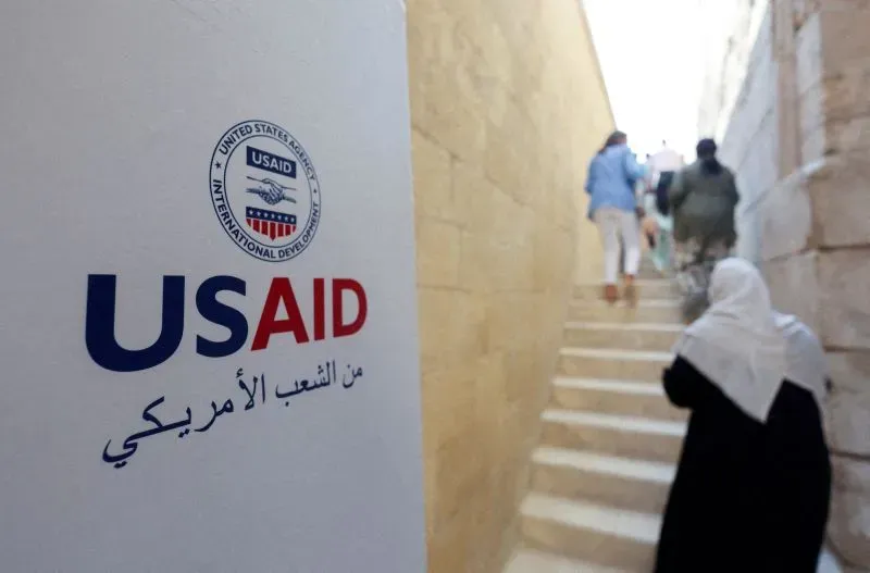 شعار الوكالة الأمريكية للتنمية الدولية (USAID) مع أشخاص يتجهون نحو الدرج، يعكس جهود المساعدات الخارجية في الدول النامية.