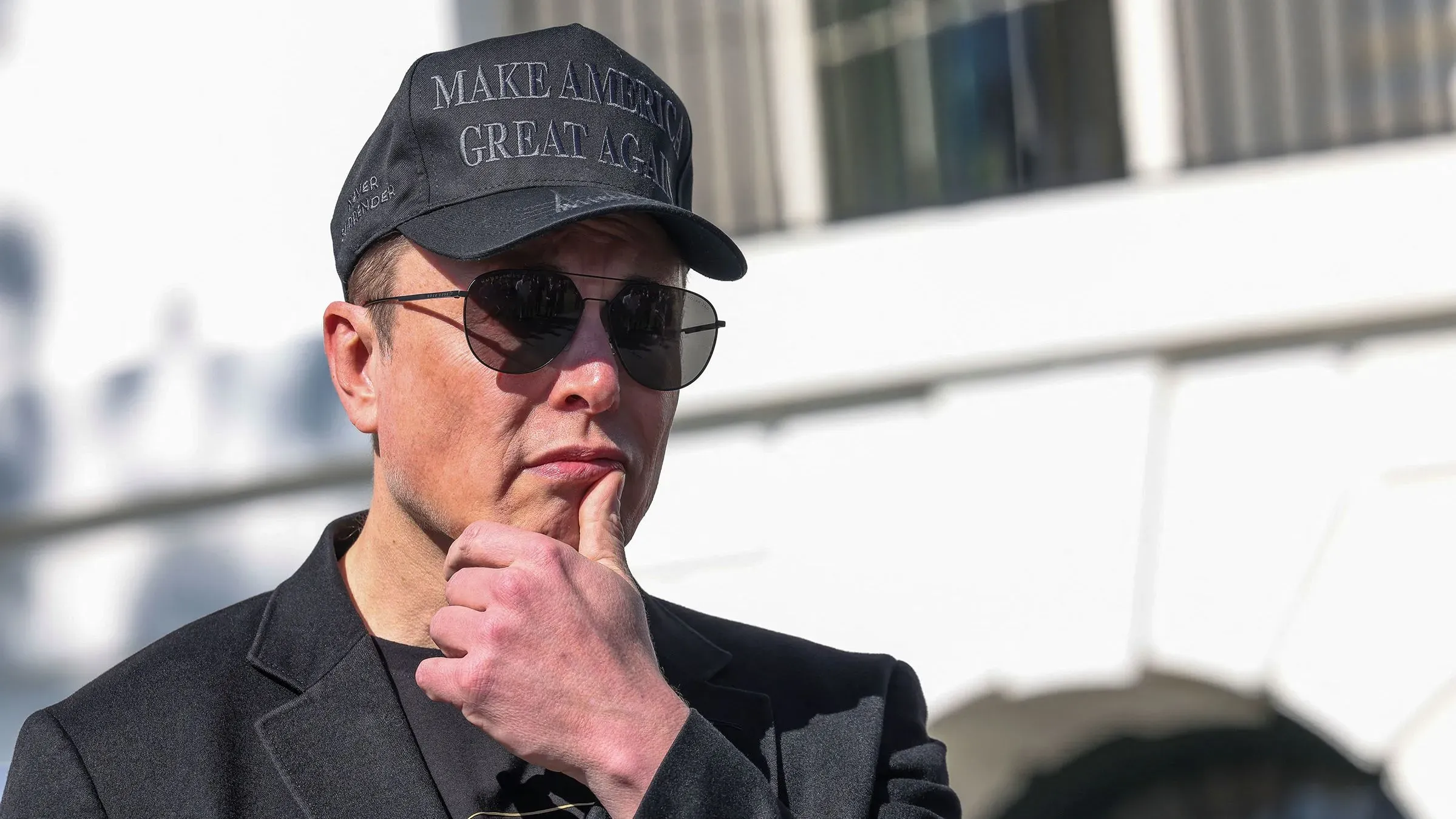 إيلون ماسك يرتدي قبعة مكتوب عليها "اجعل أمريكا عظيمة مرة أخرى" أثناء تفكيره، وسط أجواء خارجية. يزور البنتاغون لمناقشة خطط عسكرية.