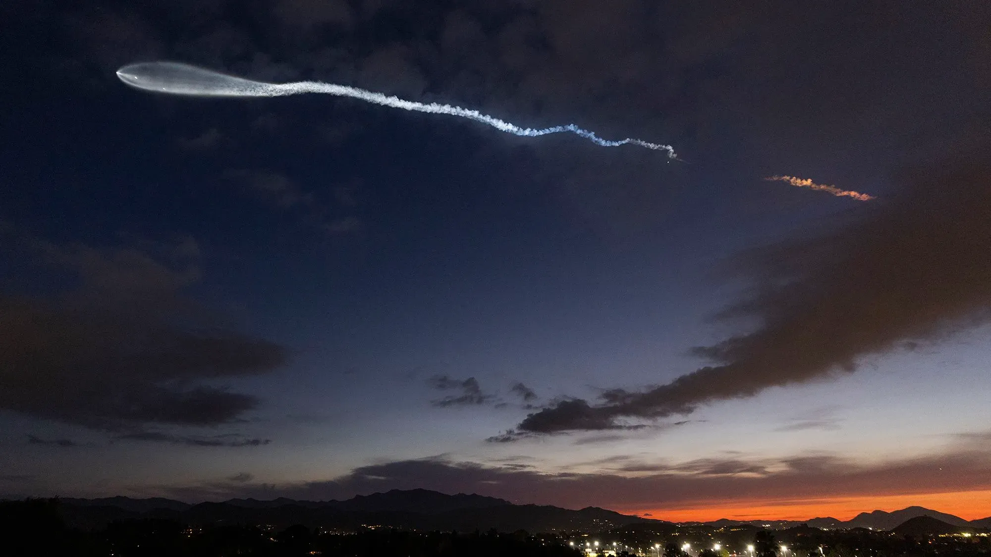 سحابة من الدخان الأبيض تمتد في السماء بعد إطلاق صاروخ SpaceX، مع غروب الشمس في الخلفية، مما يعكس جهود الشركة لتحديث تكنولوجيا الطيران.