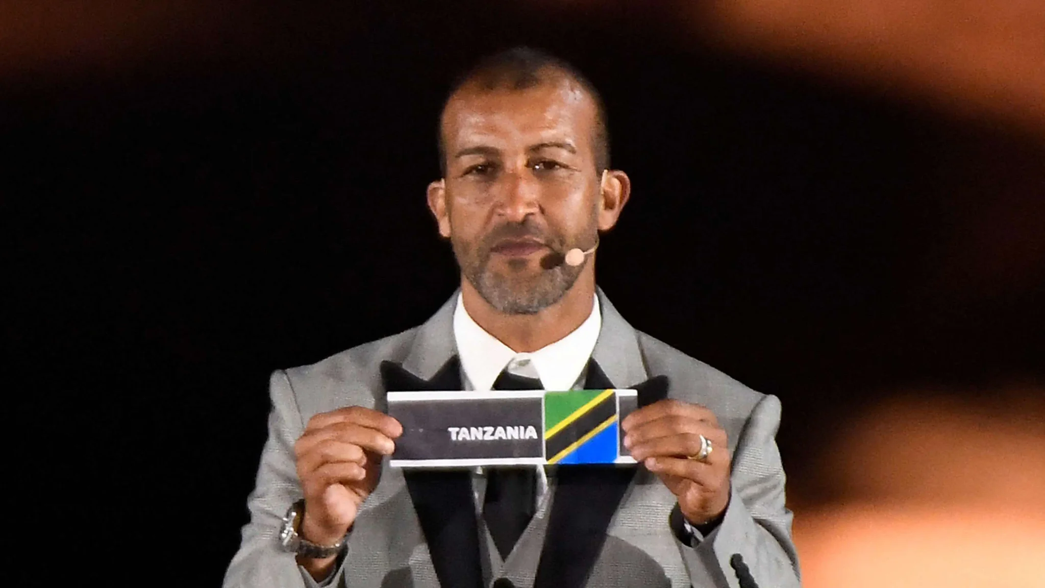 مصطفى حجي، نجم كرة القدم المغربي السابق، يحمل بطاقة فريق تنزانيا خلال قرعة كأس أمم أفريقيا 2025، في سياق الحديث عن نزاع اللقب بين المغرب والسنغال.
