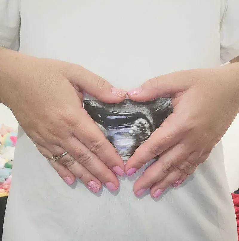 صورة تظهر يدي امرأة حامل تشكلان قلبًا حول صورة الأشعة السينية للجنين، تعبيرًا عن الأمل والقلق بشأن حقوق الأطفال المولودين في الولايات المتحدة.