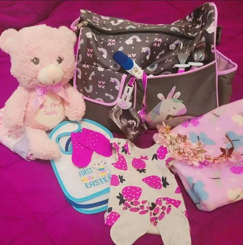 صورة تحتوي على حقيبة للأمومة تتضمن دمى ولعبة دب، ملابس أطفال ومستلزمات جديدة، تعكس مخاوف الأمهات الحوامل في ظل التغيرات القانونية المتعلقة بالمواطنة.