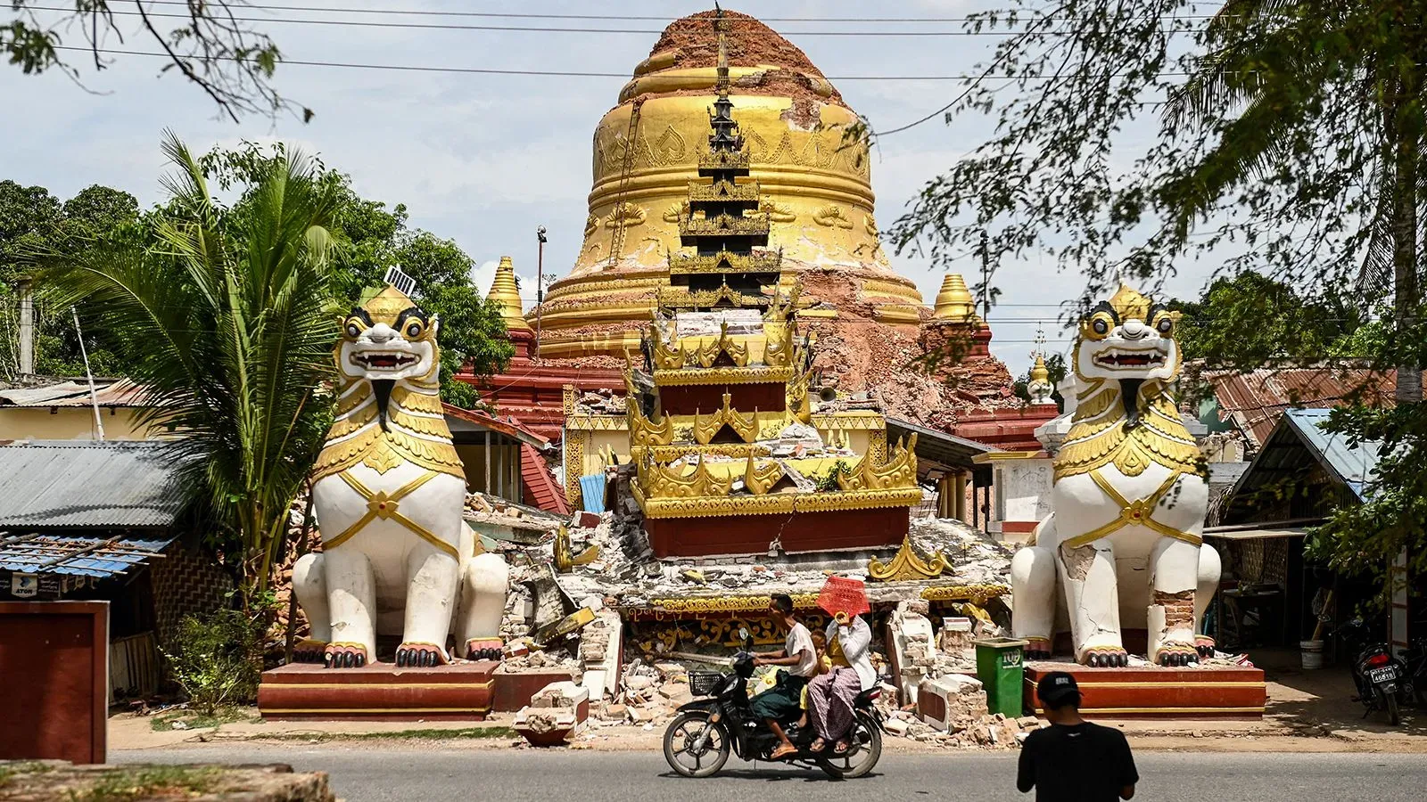 تظهر الصورة معبدًا في ميانمار تعرض لدمار كبير بعد زلزال قوي، مع تمثالين أسدين على الجانبين، وناس يسيرون في الشارع.