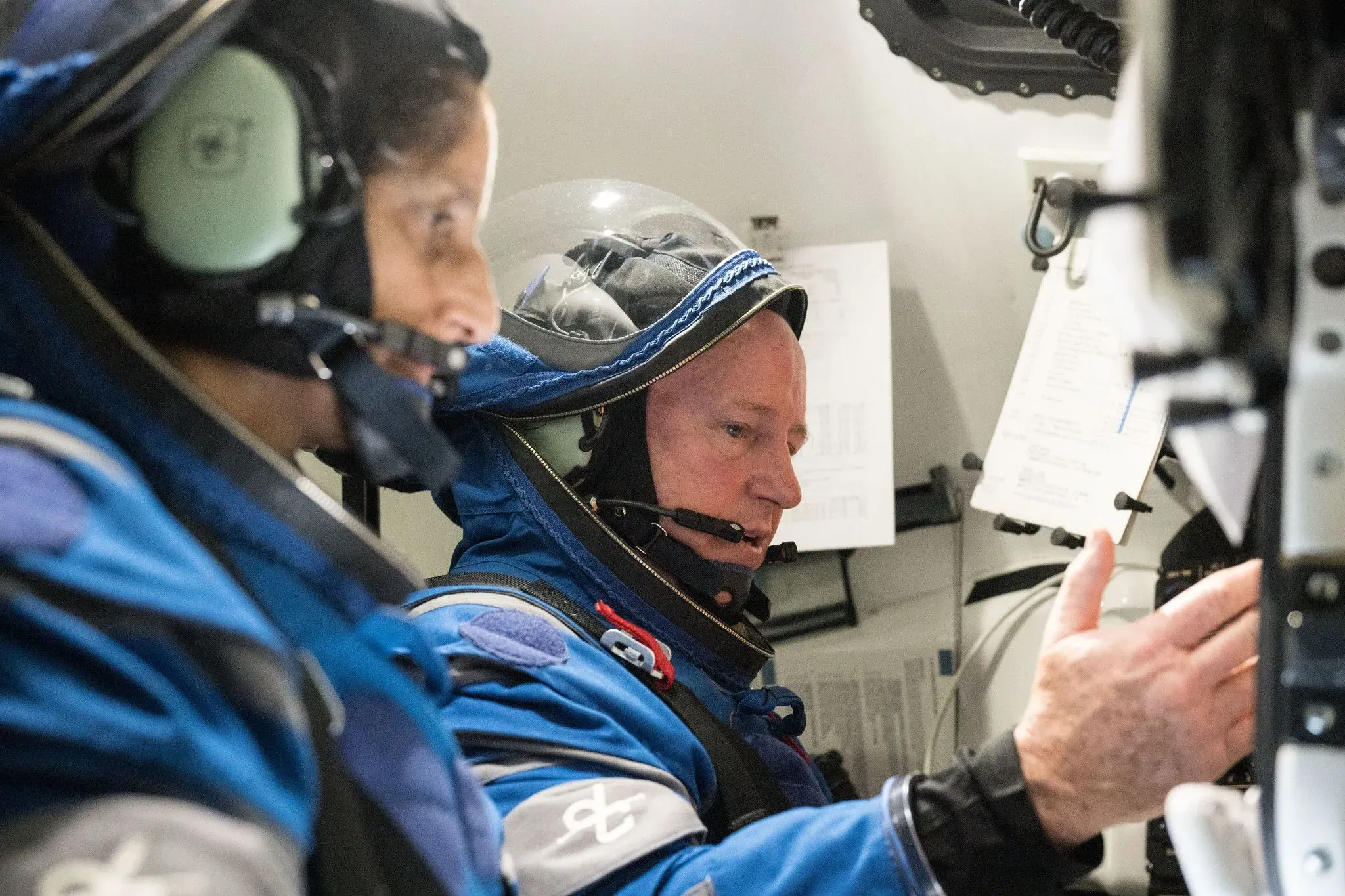 رائد الفضاء بوتش ويلمور وسوني ويليامز يرتديان بدلات فضائية داخل مركبة فضائية، يستعدان لمهمة فضائية معقدة.