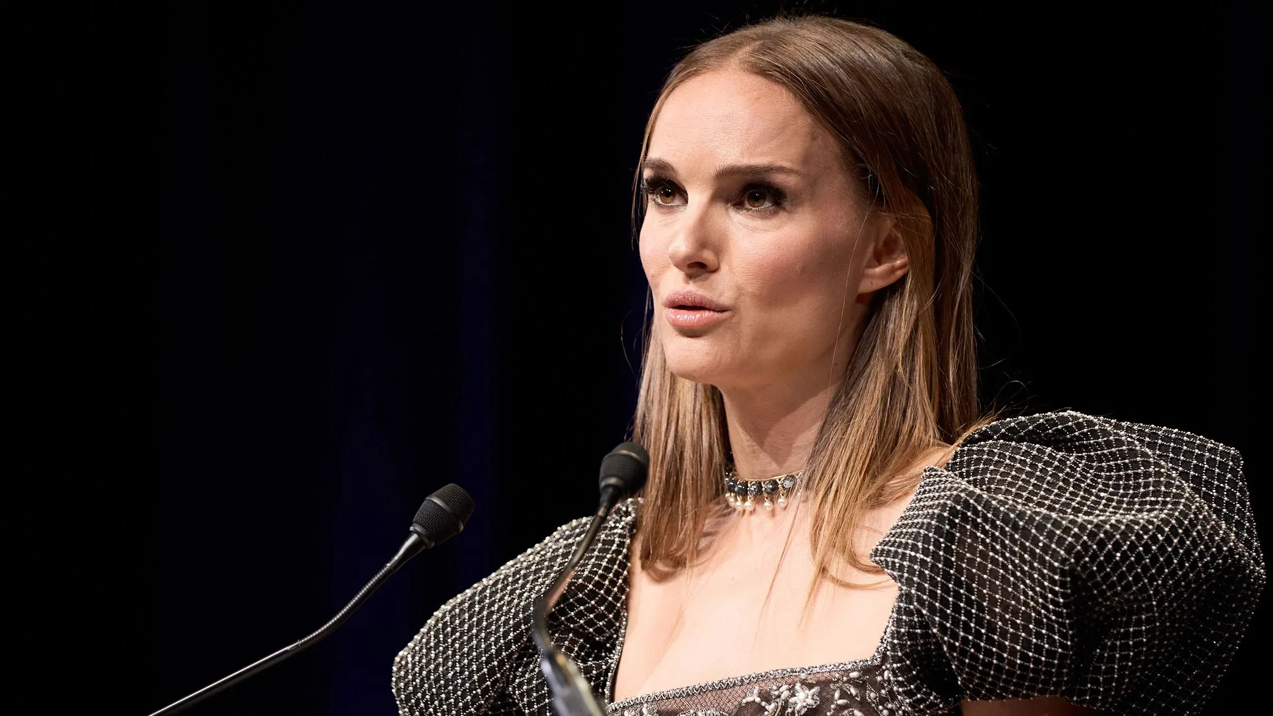 ناتالي بورتمان تتحدث في حدث عام، مرتدية فستان أنيق، تعبر عن تجربتها كنجمة منذ الطفولة وتحدياتها في هوليوود.