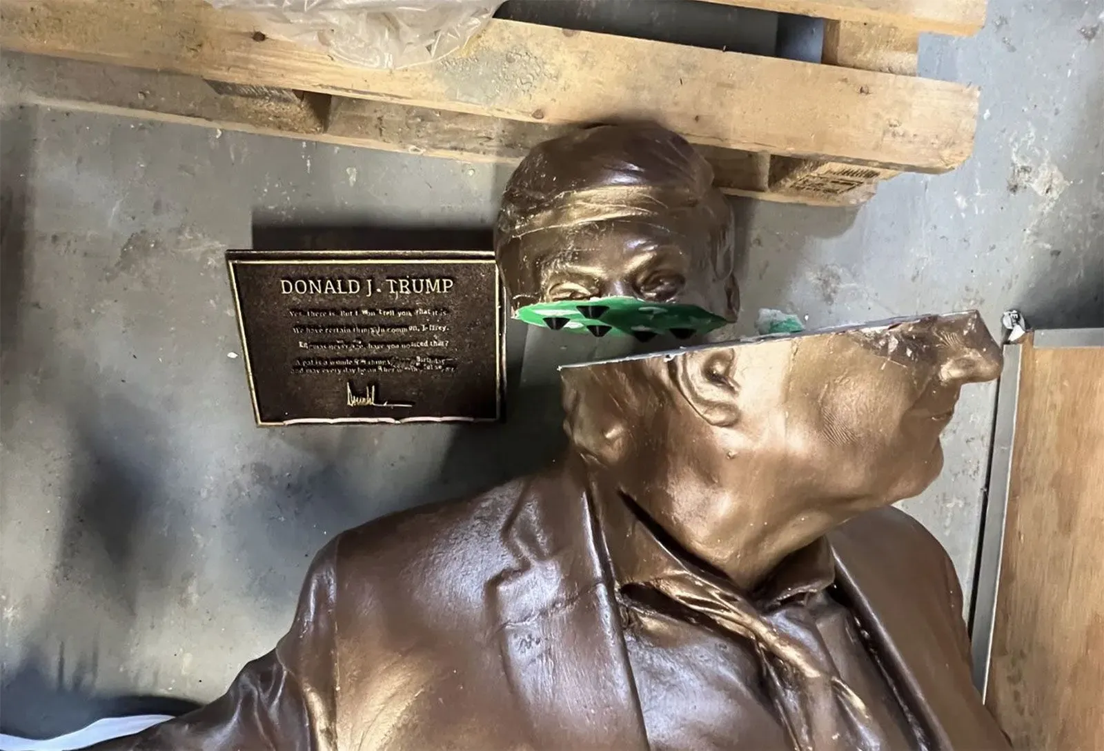 تمثال تالف للرئيس دونالد ترامب، يظهر مقطعًا مكسورًا من رأسه، مع لوحة تحمل اسمه، مما يعكس الجدل حول حريّة التعبير.