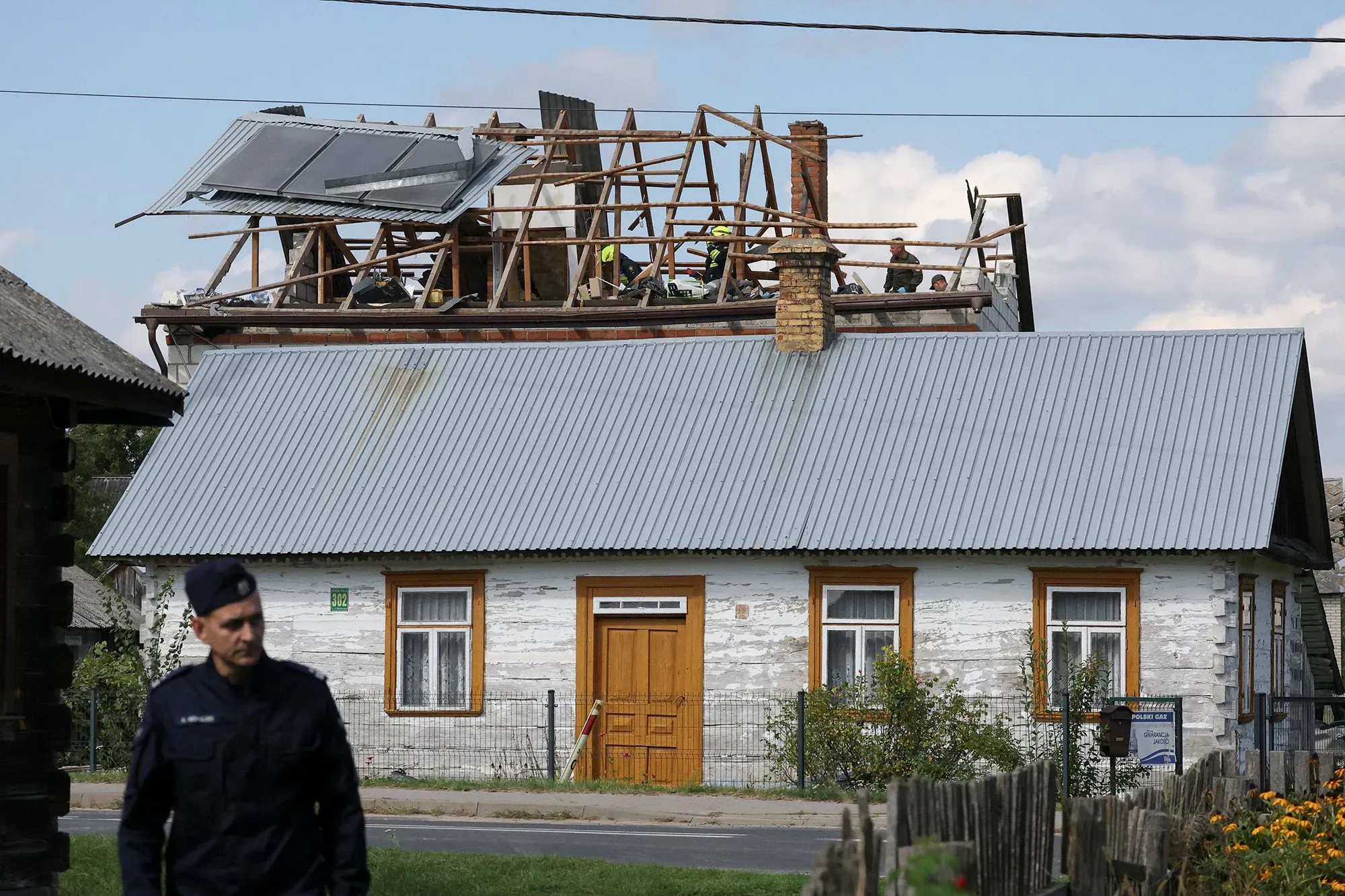 رجال إطفاء يعملون على إصلاح سقف منزل تضرر، مع وجود آثار دمار واضحة. الصورة تعكس تأثير الطائرات بدون طيار الروسية على المناطق السكنية.