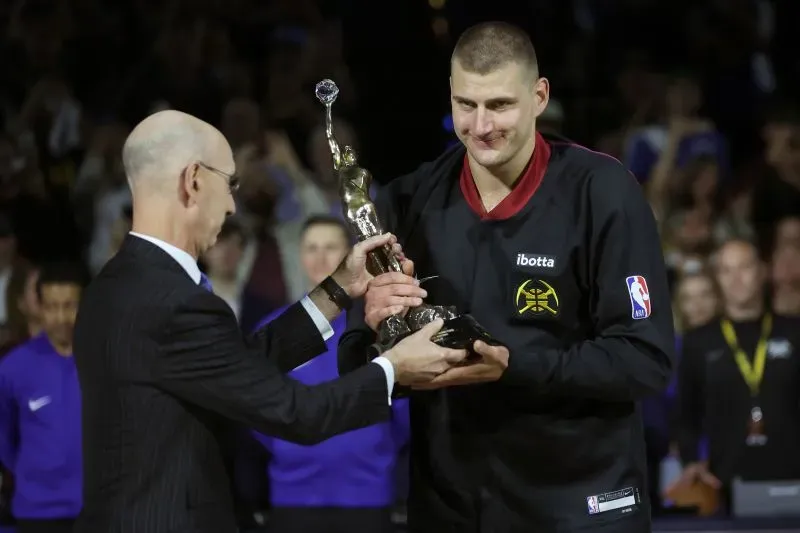 لاعب كرة سلة يتسلم جائزة MVP من مفوض الدوري الأمريكي للمحترفين، مع جمهور متحمس في الخلفية.