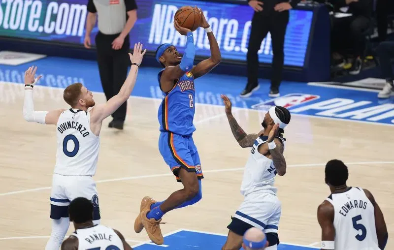 لاعب من فريق أوكلاهوما سيتي ثاندر ينفذ قفزة تسديدة في مباراة كرة سلة، مع وجود لاعبين من الفريق المنافس في محاولة للدفاع عنه.