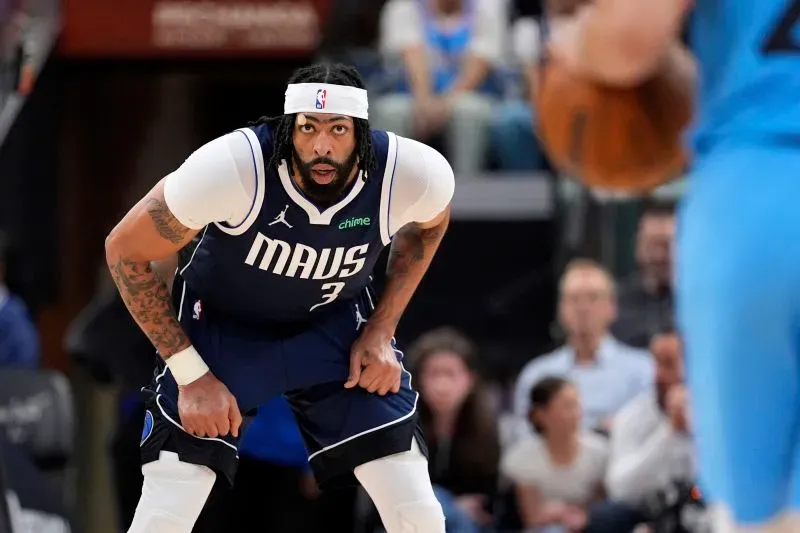 لاعب دالاس مافريكس يرتدي زي الفريق، يستعد للدفاع خلال مباراة حاسمة في الدوري الأمريكي للمحترفين، مع وجود جمهور في الخلفية.