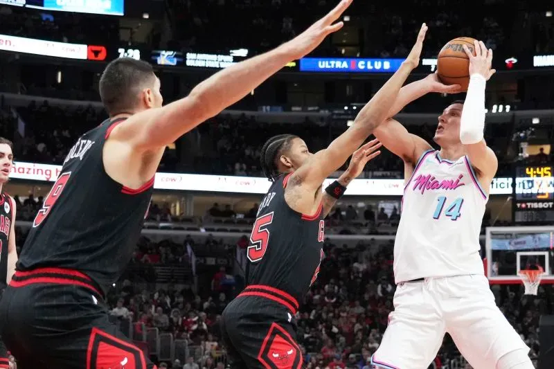 لاعب من فريق ميامي هيت يحاول تسجيل نقطة بينما يتصدى له لاعبان من فريق شيكاغو بولز، في مباراة حماسية بالدوري الأمريكي للمحترفين.