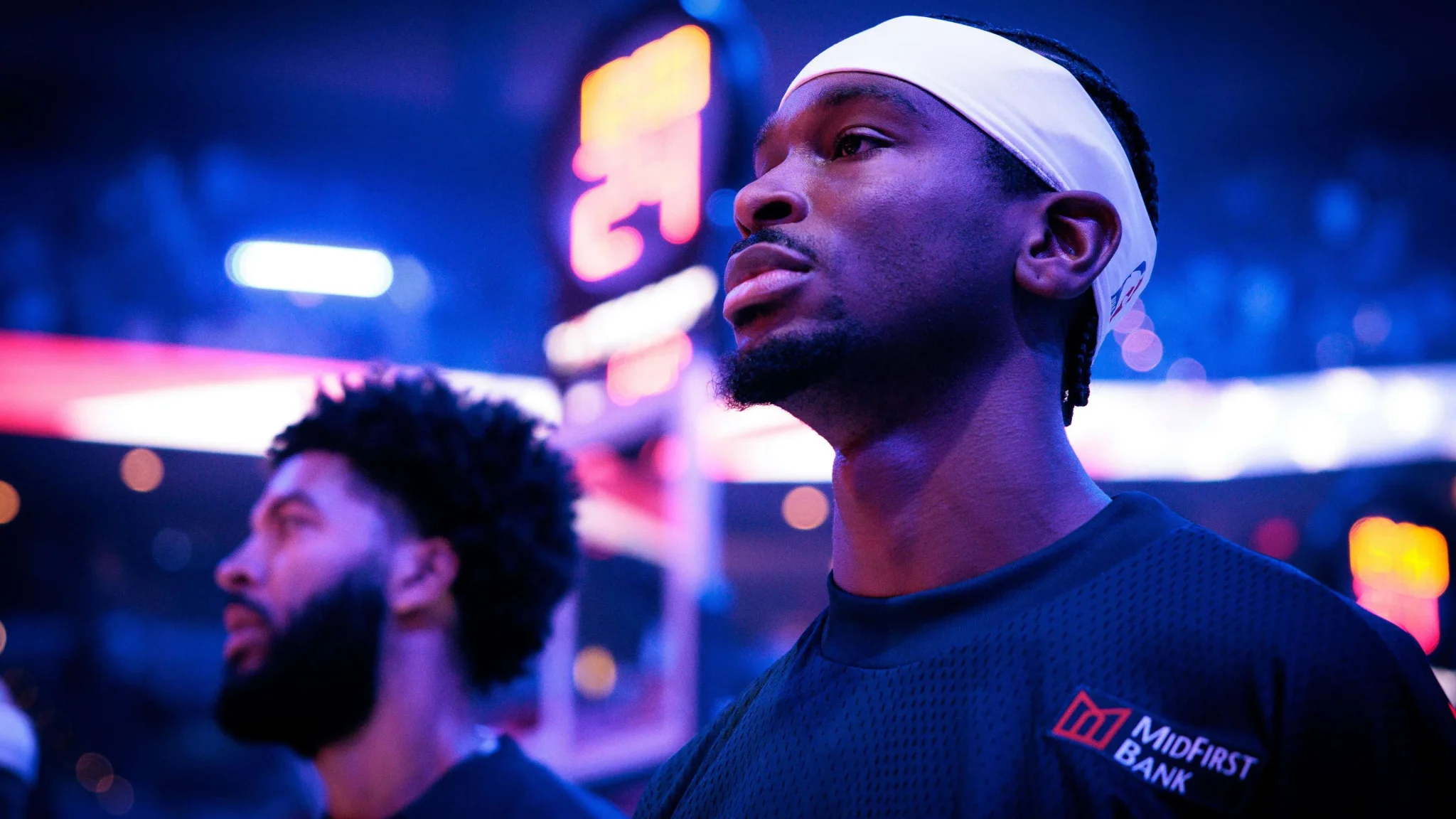 شاي جيلجوس-ألكسندر نجم NBA يرتدي زي فريقه في لحظة تركيز قبل مباراة، مع إضاءة ملعب كرة السلة في الخلفية.