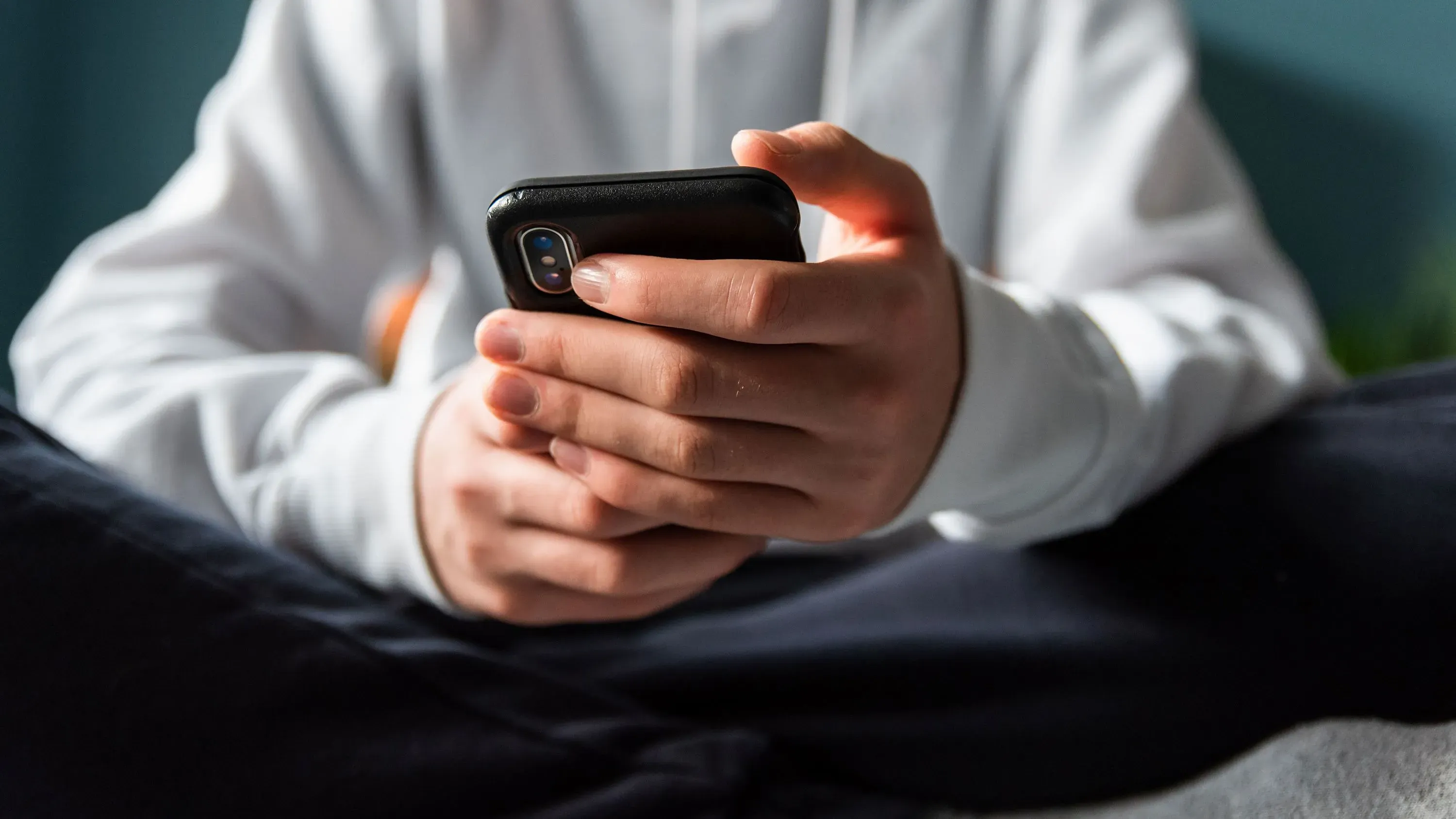 شخص يجلس على الأرض ممسكًا بهاتفه الذكي، يعكس تأثير وسائل التواصل الاجتماعي على الشباب وصحتهم النفسية.