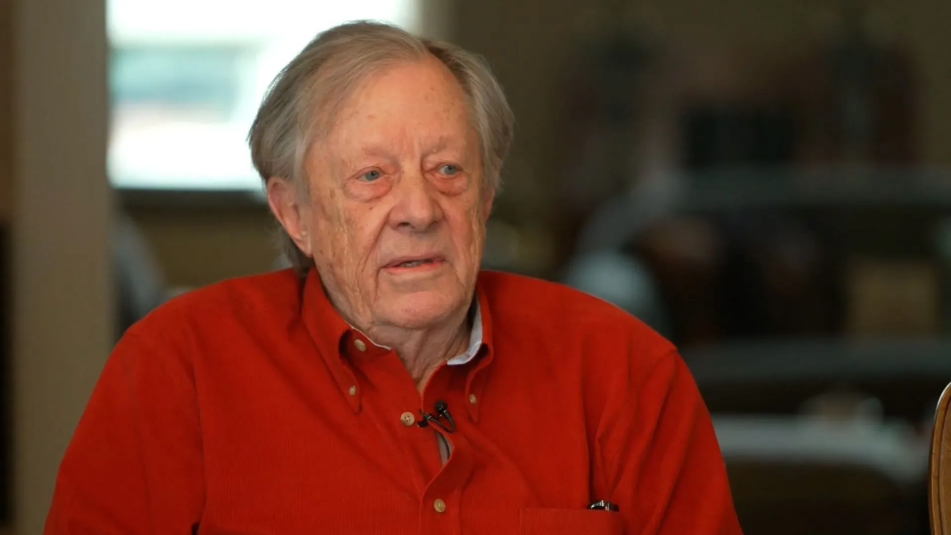 رجل مسن يرتدي قميصًا أحمر، يجلس في مكان داخلي، ويبدو في حالة تأمل، يمثل قصة نيد جونسون الذي أثبت أنه لا يزال على قيد الحياة.