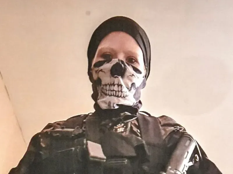 شخص يرتدي زيًا عسكريًا وقناعًا مزخرفًا برسم جمجمة، يظهر في صورة ذات إضاءة خافتة، مما يعكس أجواء التوتر المرتبطة بالتطرف.