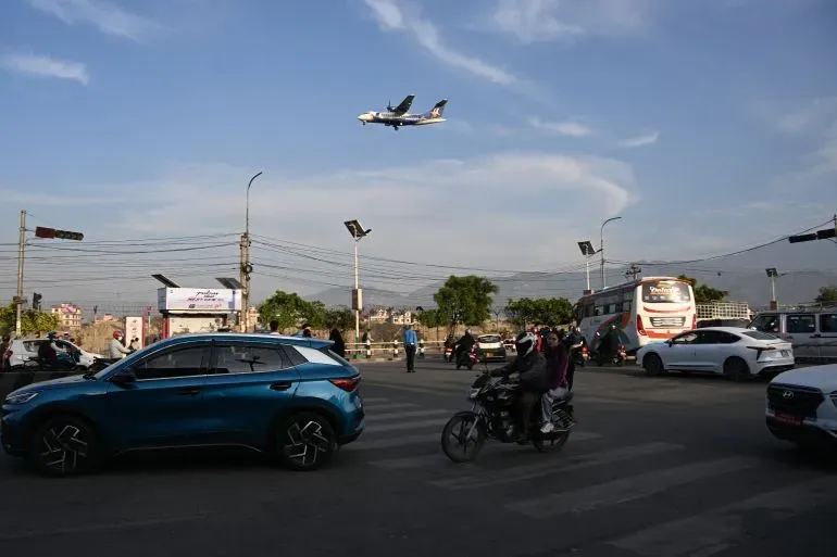 طائرة تحلق فوق تقاطع مزدحم في نيبال، حيث تتواجد سيارات ودراجات نارية، مما يعكس تأثير أزمة الوقود على حركة المرور.