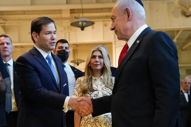 وزير الخارجية الأمريكي ماركو روبيو يصافح رئيس الوزراء الإسرائيلي بنيامين نتنياهو في اجتماع رسمي، مع وجود آخرين في الخلفية.