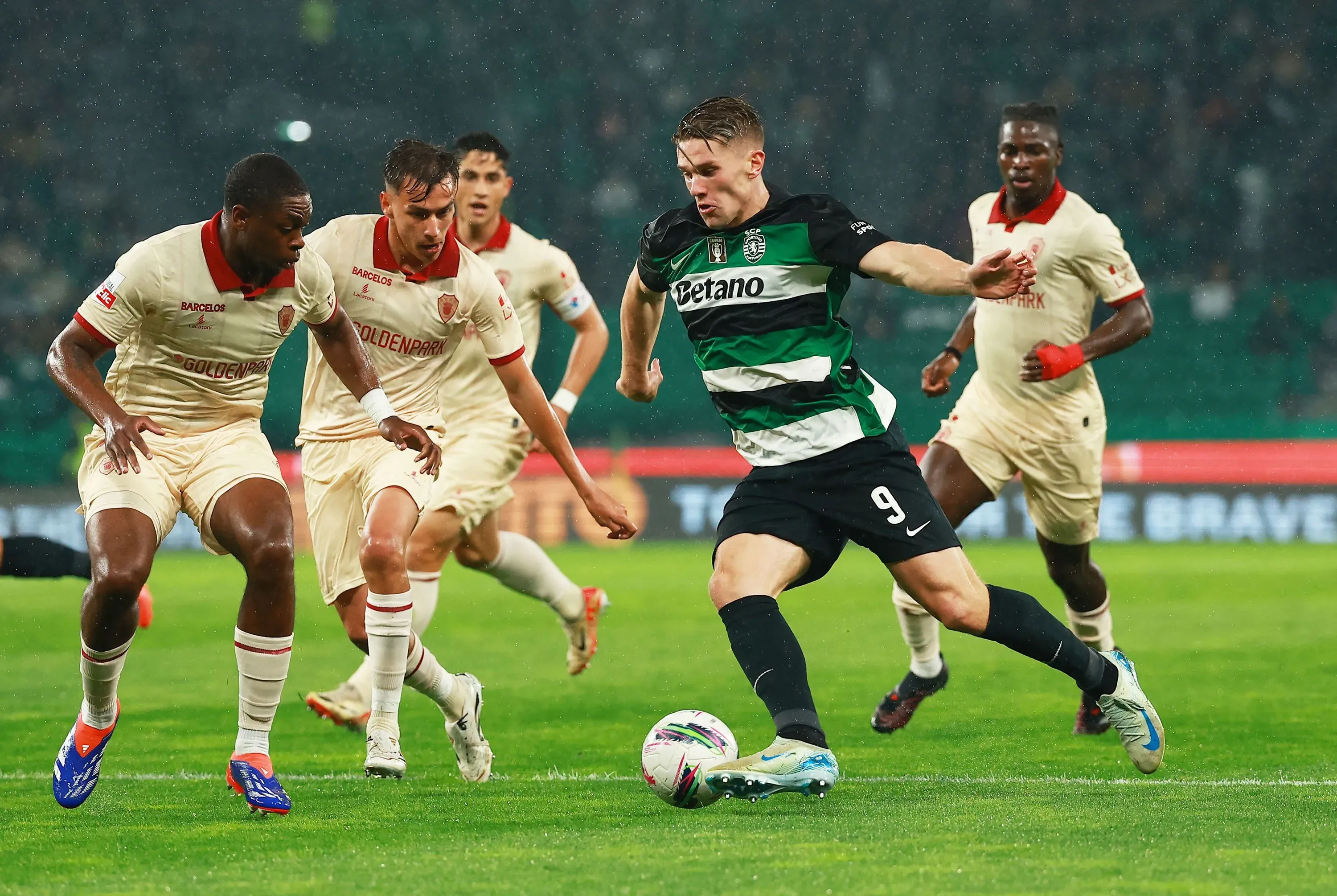 جيوكيريس، مهاجم أرسنال الجديد، يتجاوز لاعبين من الفريق المنافس خلال مباراة في الأمطار، مع التركيز على قدراته الهجومية.