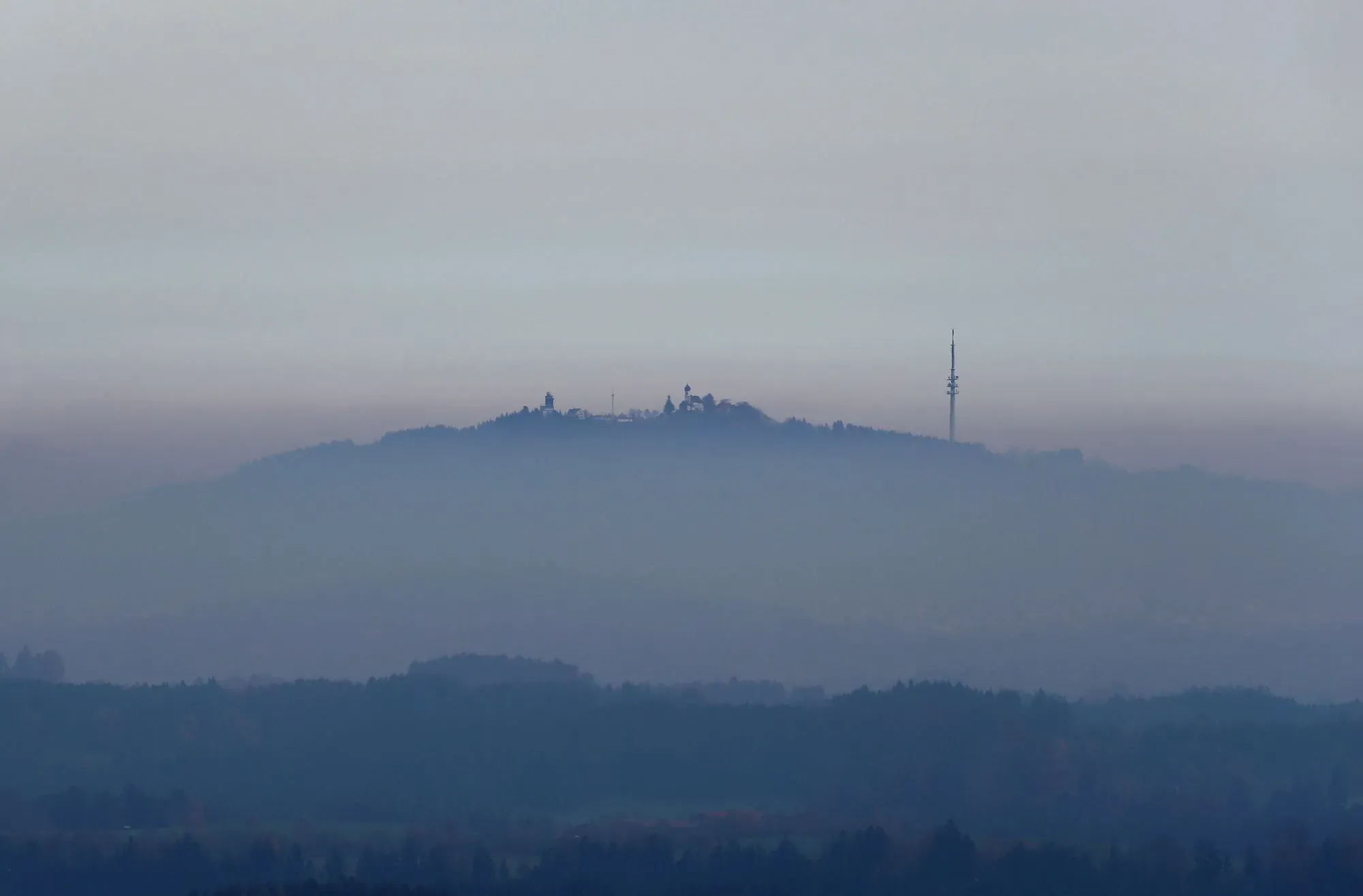 منظر لجبل مغطى بالضباب، يظهر في الخلفية برج اتصالات، مما يعكس تأثير التلوث على البيئة.