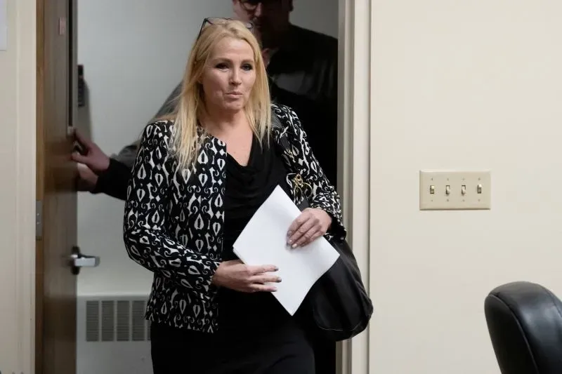 امرأة ترتدي سترة مزخرفة تحمل أوراقًا، تخرج من غرفة في المحكمة، في سياق قضية القتل ضد برايان كوهبرغر.