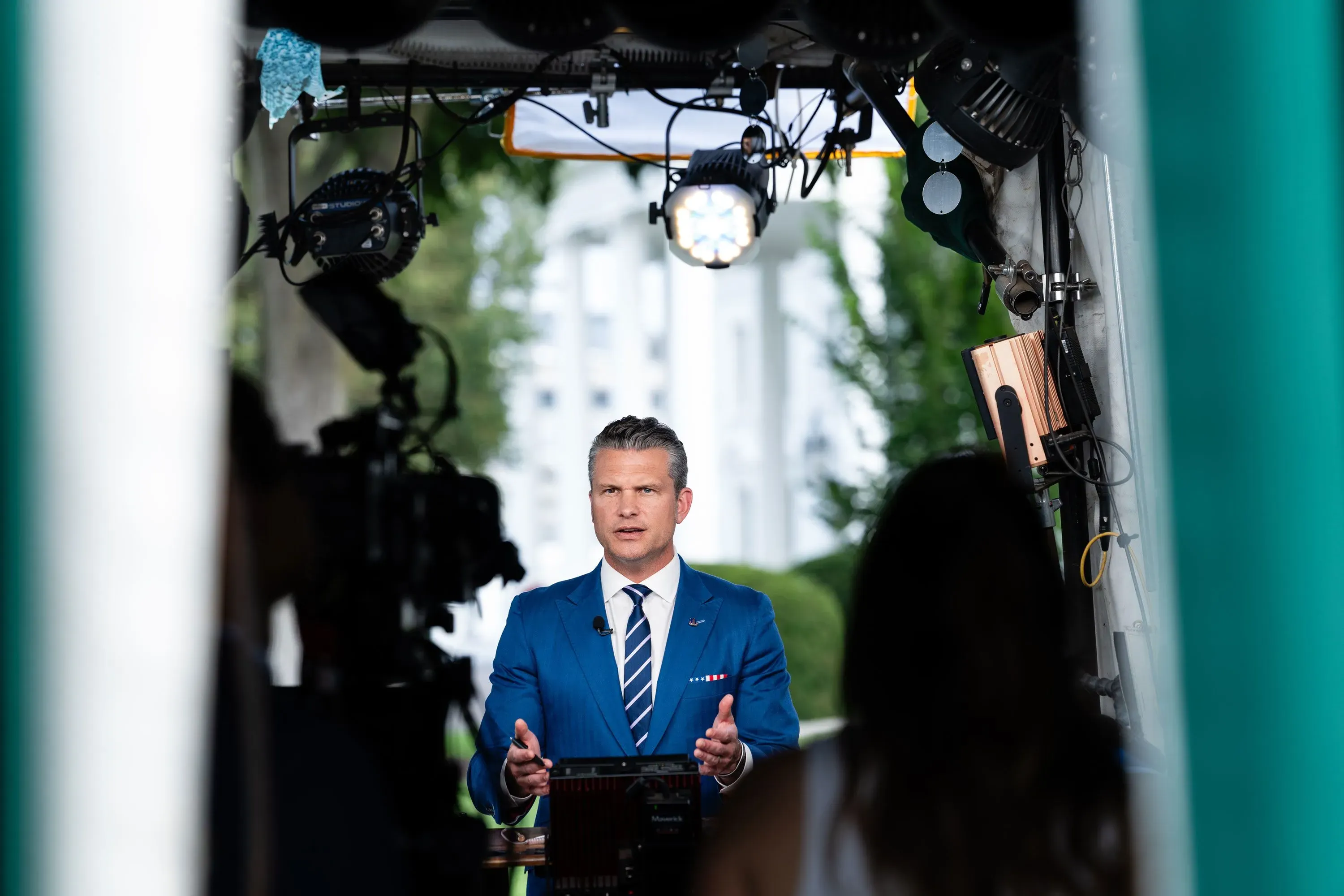 مراسل يتحدث أمام الكاميرا في موقع تصوير خارجي بالقرب من البيت الأبيض، مع تسليط الضوء على أهمية الدعم العسكري لأوكرانيا.