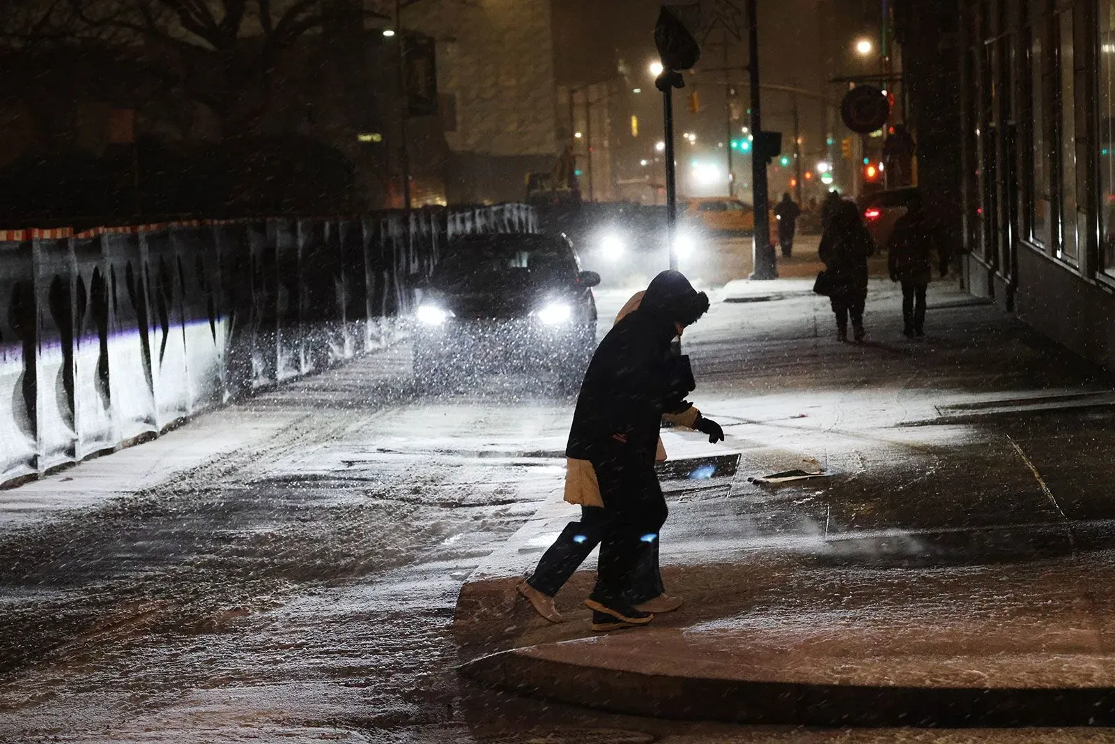 تساقط الثلوج الكثيفة في مدينة نيويورك، حيث يتجول الناس في أجواء عاصفة شتوية، مع رؤية السيارات في الخلفية.