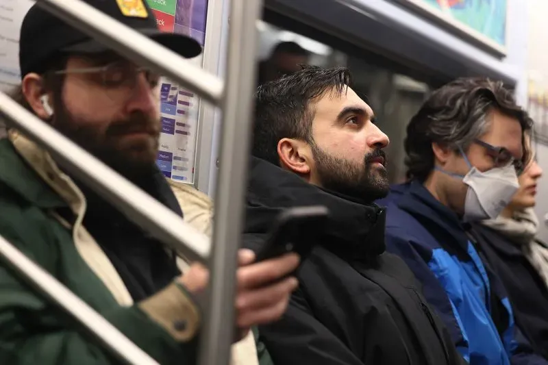 مجموعة من الركاب في مترو أنفاق نيويورك، حيث يظهر رجل يرتدي سترة داكنة ويستخدم هاتفه، بينما الآخرون يجلسون في هدوء.