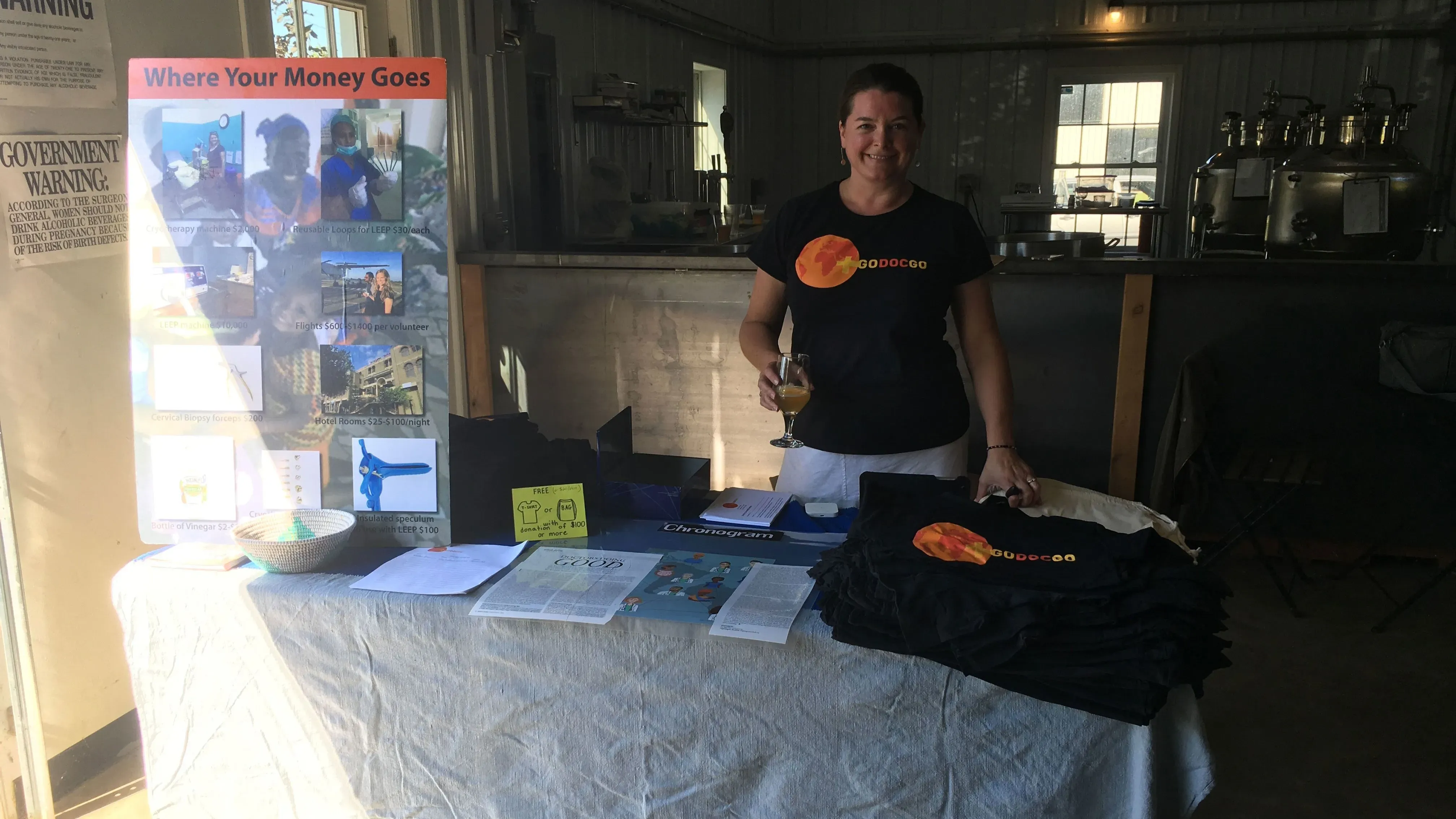 امرأة تحمل كأسًا، تقف أمام طاولة مغطاة بقماش، حيث تعرض مواد توعوية حول الرعاية الصحية الإنجابية وحقوق الإجهاض.