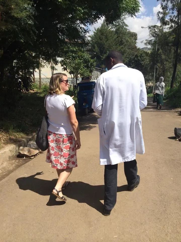 امرأة تسير بجانب طبيب يرتدي معطفاً أبيض في شارع محاط بالأشجار، يعكس التعاون في تقديم الرعاية الصحية.