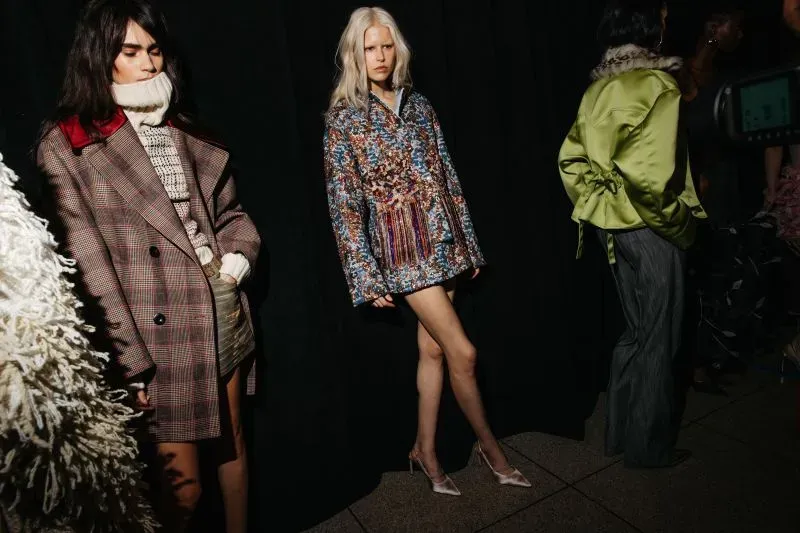 عارضات أزياء يرتدين تصاميم متنوعة خلف الكواليس خلال أسبوع الموضة في نيويورك، مع التركيز على الأزياء العصرية والمبتكرة.