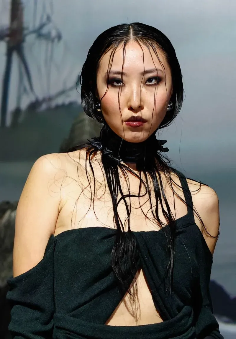 عارضة أزياء تظهر بإطلالة مميزة مع شعر مبلل وملابس داكنة، تعكس تأثيرات البحر والمسرح في أسبوع الموضة بنيويورك.