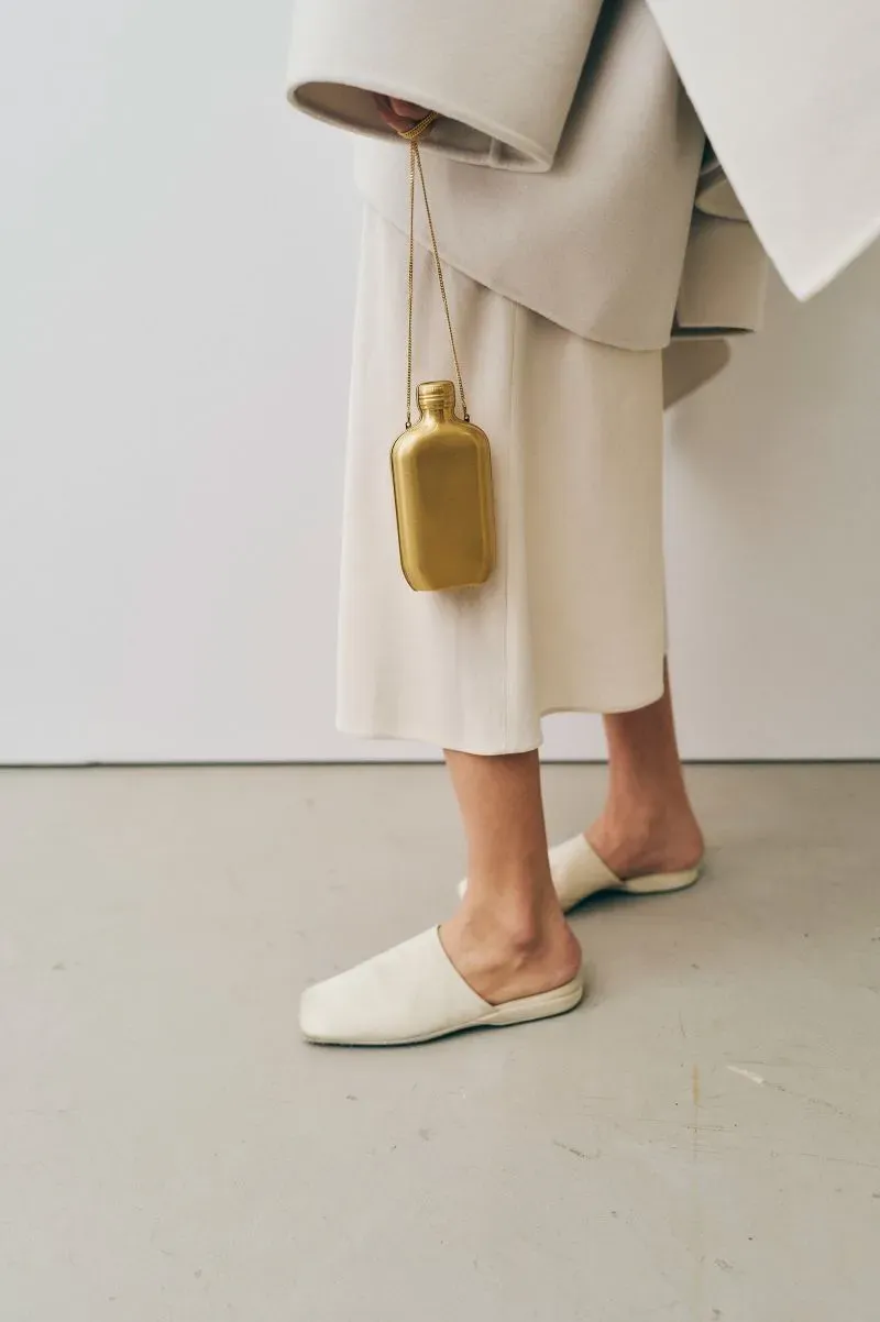 تصميم عصري يتضمن سترة بيضاء واسعة وسروال أبيض، مع حقيبة ذهبية معلقة، تعكس أسلوب الموضة الأمريكية المعاصر.