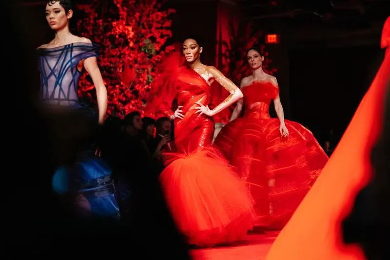 عرض أزياء في نيويورك يظهر عارضات يرتدين فساتين حمراء مبهرة، مع تصاميم أنيقة ومبهجة تعكس أحدث صيحات الموضة.