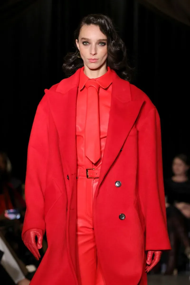 عارضة أزياء ترتدي ملابس حمراء جريئة، تشمل سترة ومعطف طويل، أثناء عرض أزياء في أسبوع الموضة في نيويورك.