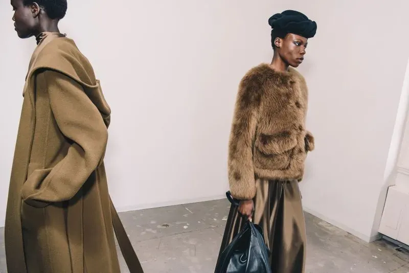 عارضتان ترتديان أزياء أنيقة خلال عرض أزياء في نيويورك، حيث تظهر إحداهما بفستان طويل بلون بني والآخرى بسترّة فروية، مما يعكس الاتجاهات الحديثة في الموضة.