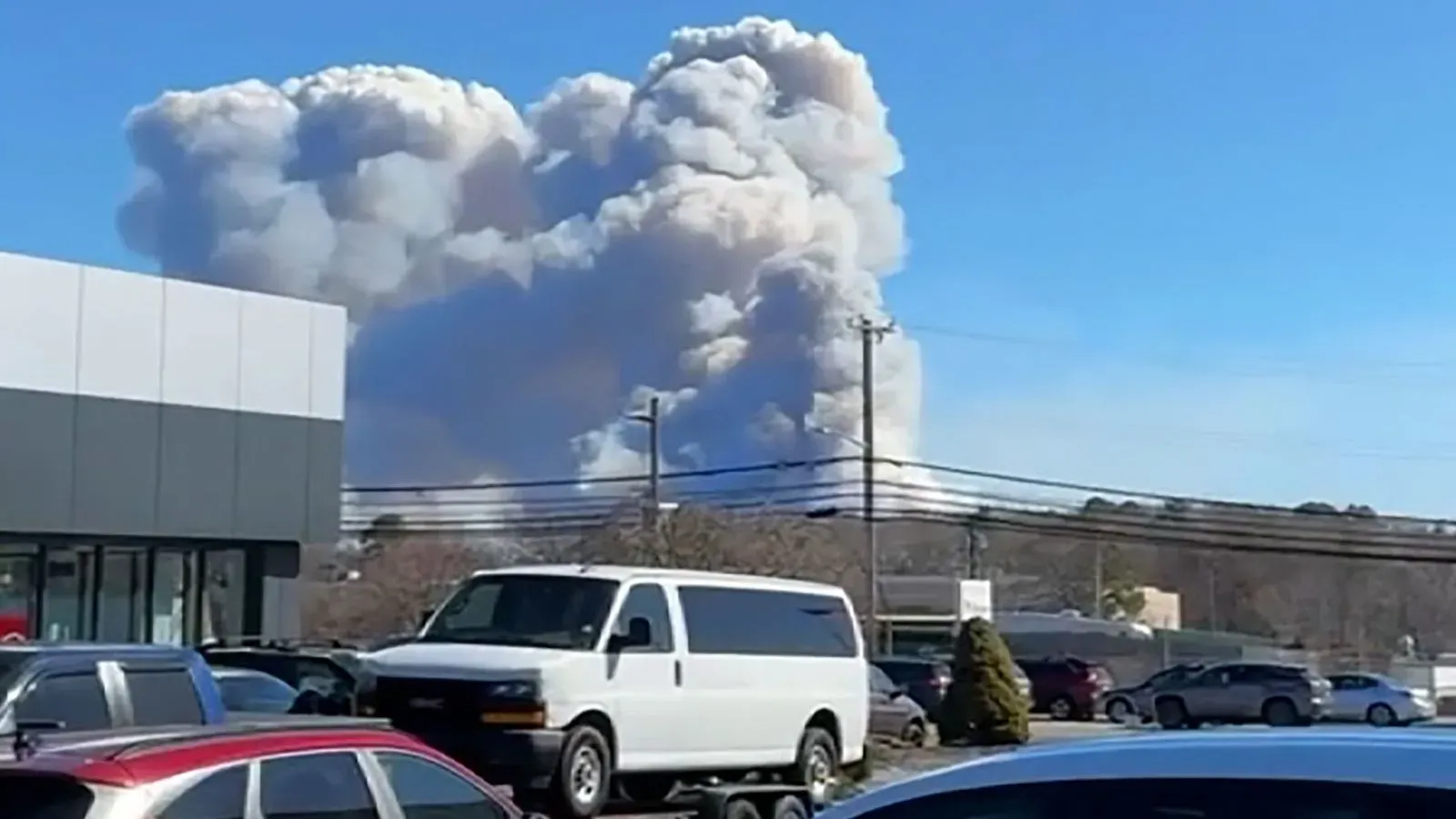 أعمدة دخان كثيفة تتصاعد في السماء نتيجة حرائق في لونغ آيلاند، مع وجود سيارات متوقفة في المقدمة، مما يعكس حالة الطوارئ.