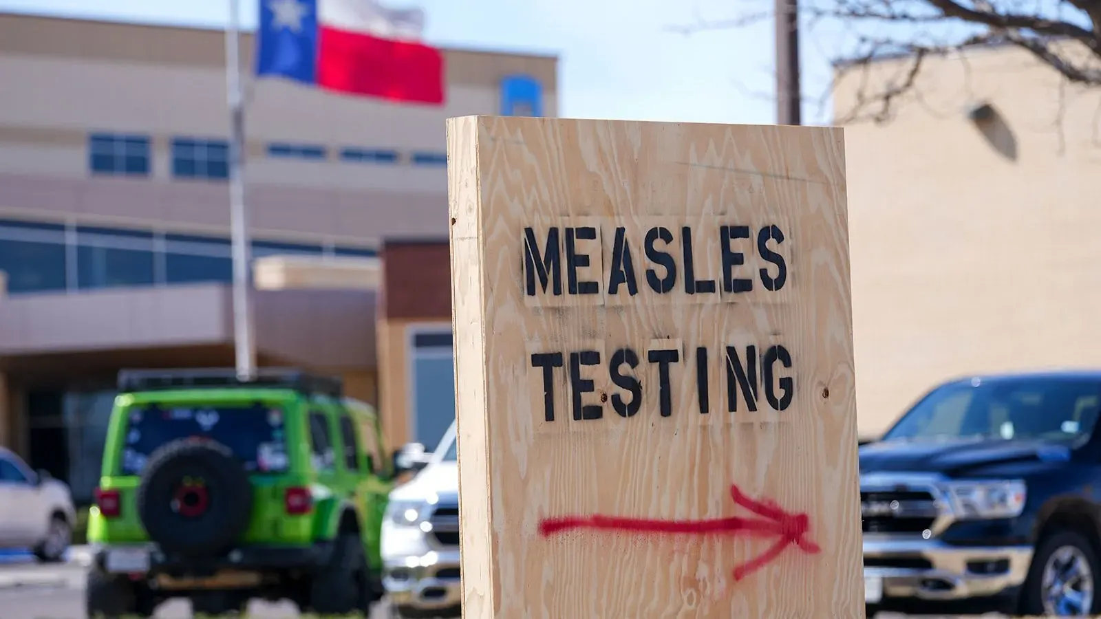 لافتة خشبية تشير إلى اختبار الحصبة، مع وجود علم تكساس في الخلفية، تعكس تفشي الحصبة في الولاية.