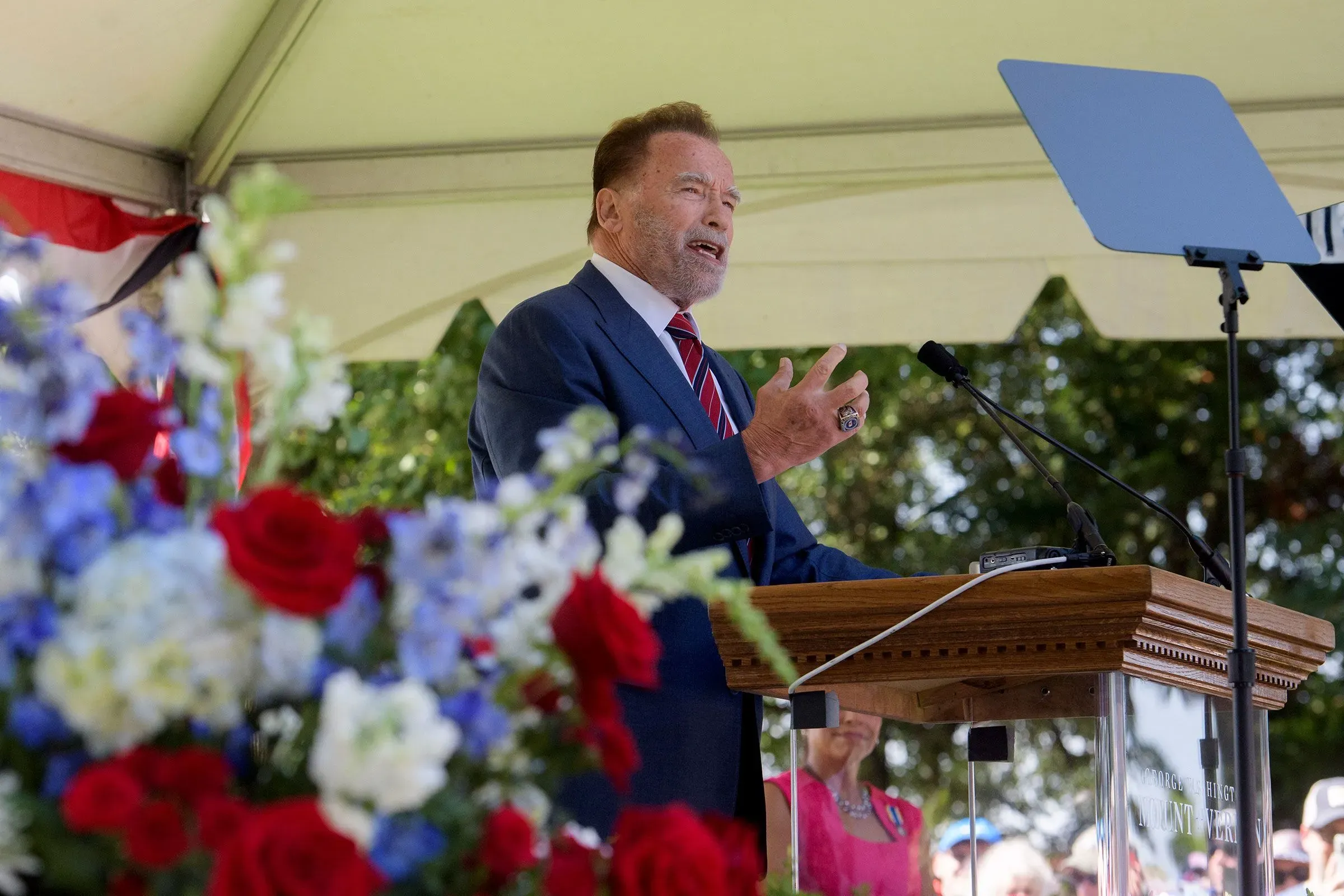 أرنولد شوارزنيجر يتحدث في حدث عام، محاطًا بزهور ملونة، مع التركيز على دعوته لإصلاحات إعادة تقسيم الدوائر الانتخابية في كاليفورنيا.