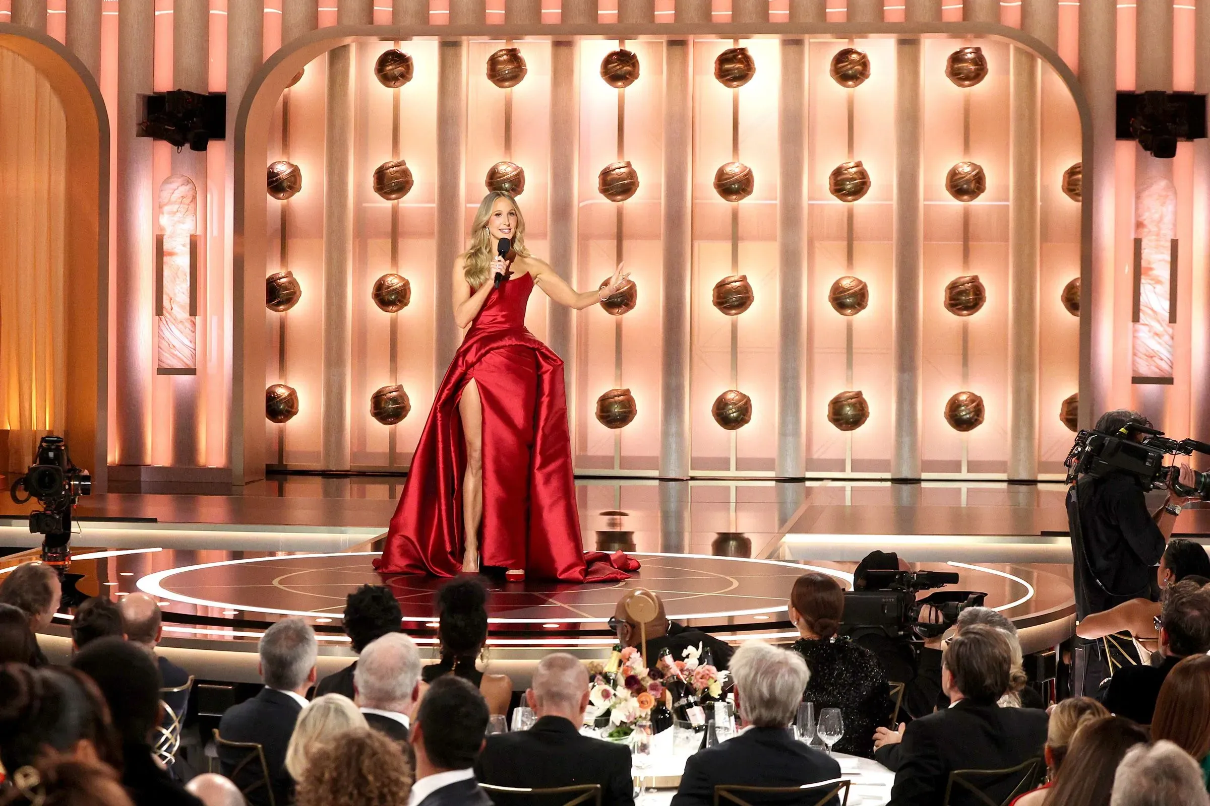 نيكي جلاسر تقدم عرضها في حفل توزيع جوائز غولدن غلوب 2026، مرتدية فستانًا أحمر، بينما يستمع الجمهور إلى نكاتها.