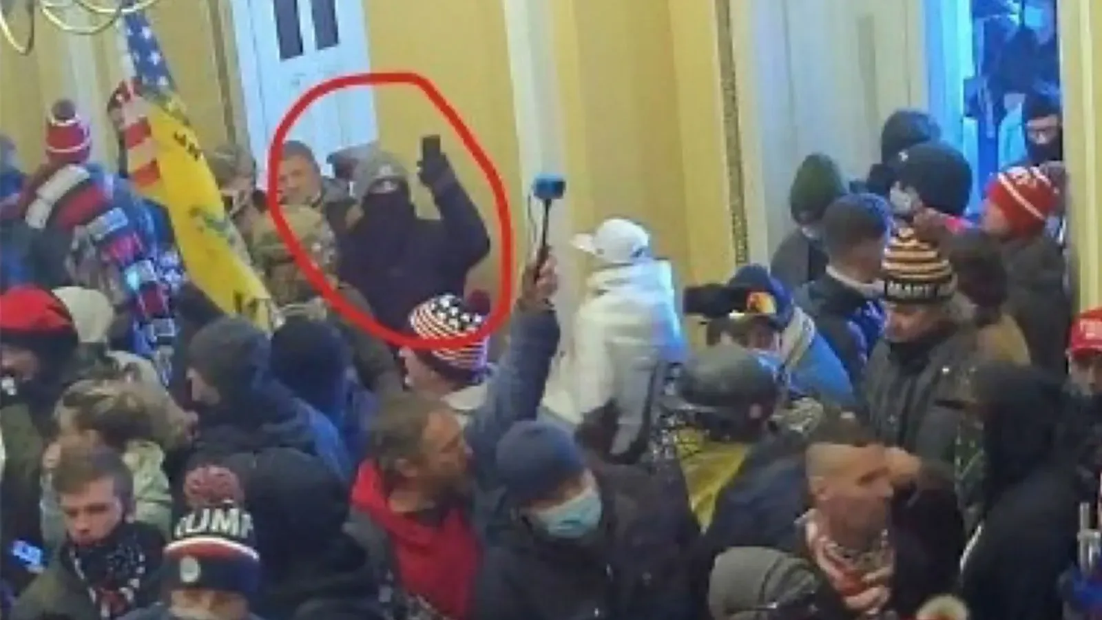 مجموعة من الأشخاص داخل مبنى الكابيتول الأمريكي خلال أحداث الشغب في 6 يناير 2021، مع شخص يحمل هاتفًا في المقدمة.