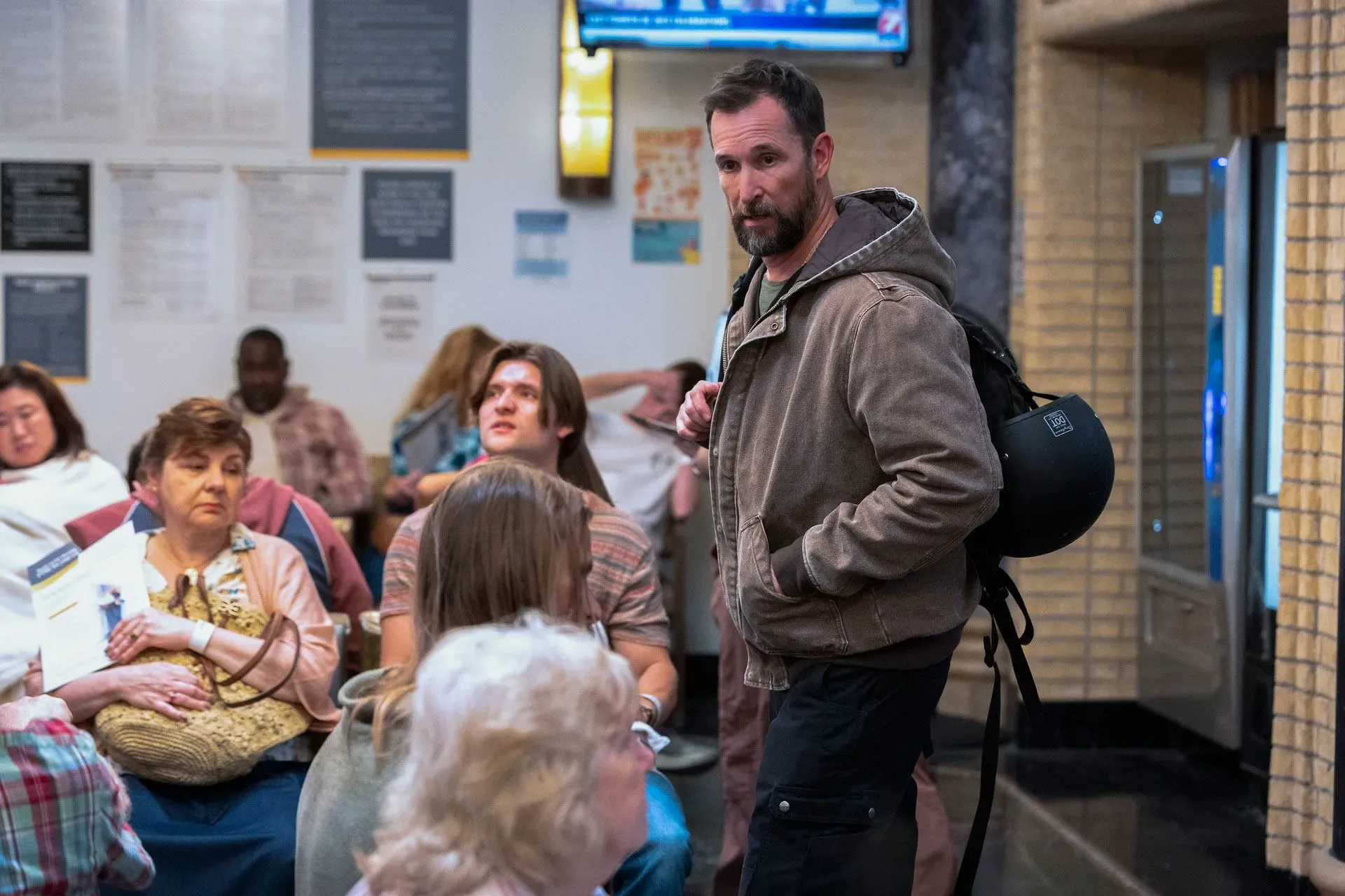 مشهد من المسلسل "ذا بيت" يظهر الدكتور روبي وسط مرضى ينتظرون في قسم الطوارئ، مع التركيز على التوترات في بيئة العمل.